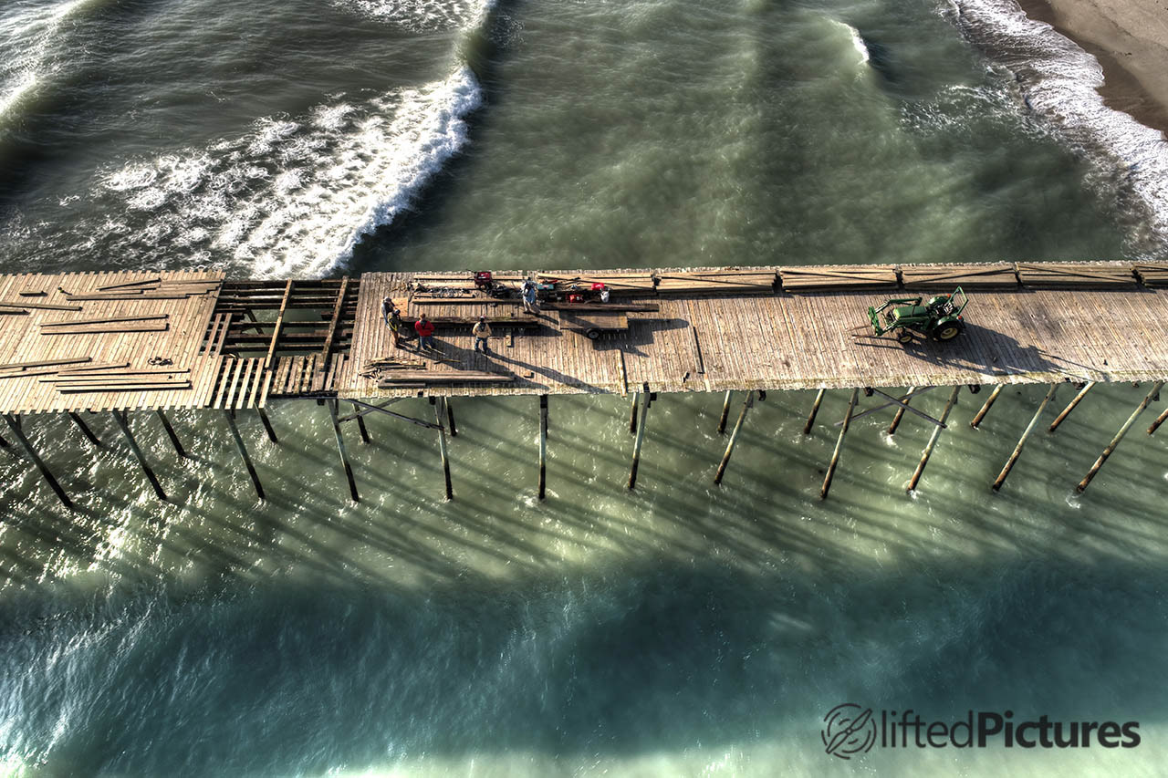 Workers and a tractor on the Kure Beach pier, with the ocean below the deck