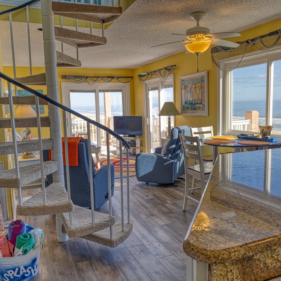 Bright coastal short-term rental interior with ocean views, spiral staircase, and beach decor — STR photography by Lifted Pictures